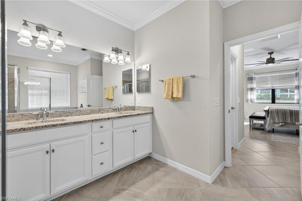 Ensuite bathroom featuring double vanity, crown molding, a ceiling fan, light tile patterned floors, and an enclosed shower