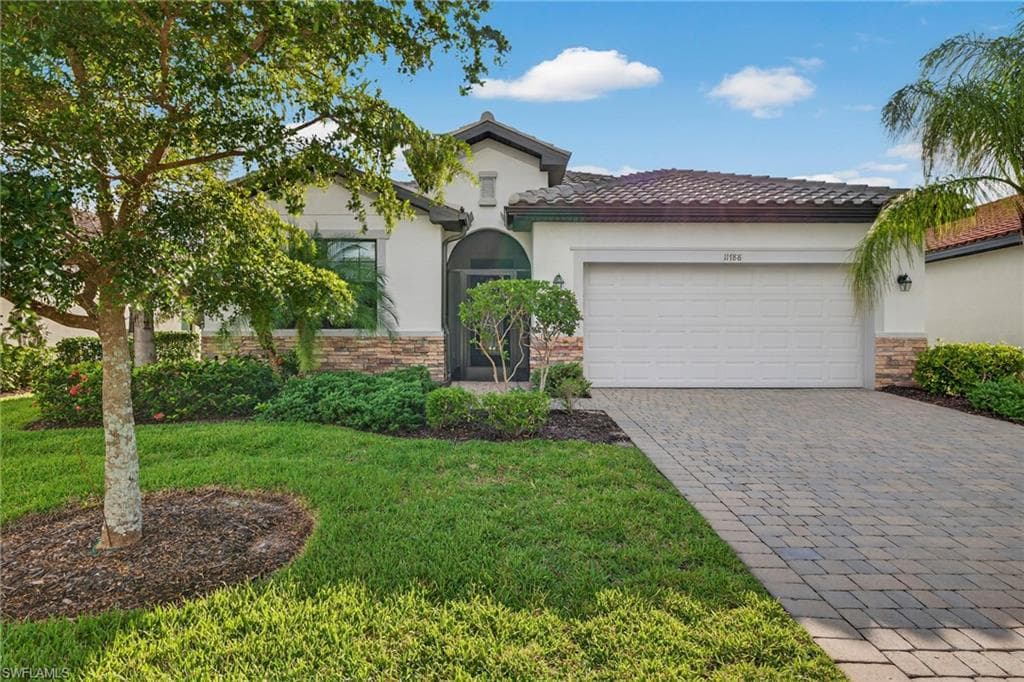 View of front of home featuring stone siding, stucco siding, decorative driveway, a front lawn, and a tiled roof