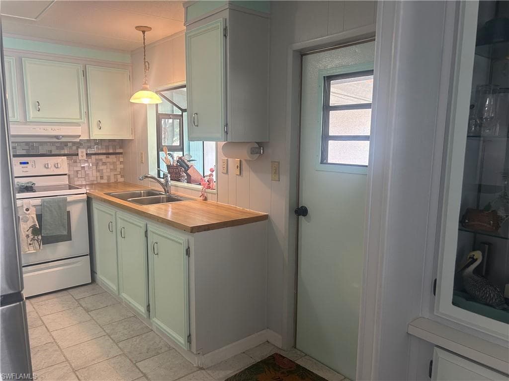 Kitchen featuring green cabinets, pendant lighting, white electric range oven, backsplash, and plenty of natural light