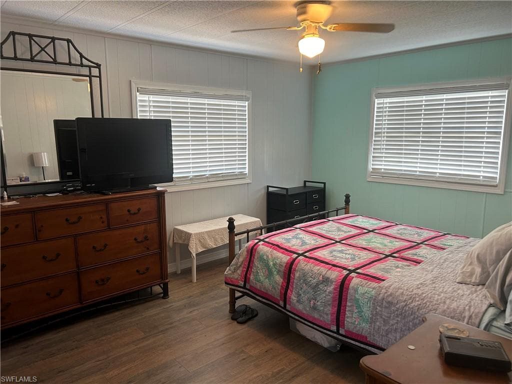 Bedroom featuring dark wood finished floors, ceiling fan, and wooden walls