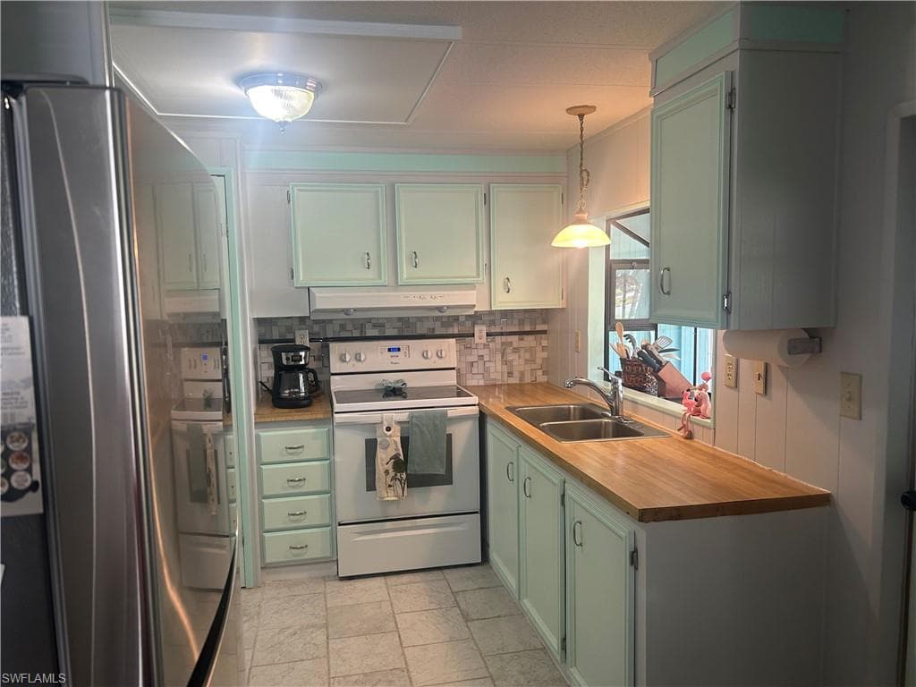 Kitchen featuring green cabinets, stainless steel refrigerator, white range with electric cooktop, hanging light fixtures, and light countertops