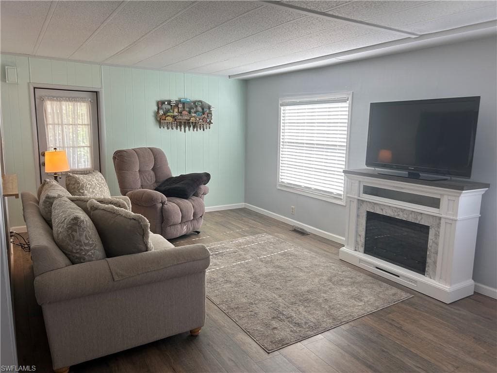 Living room featuring wood finished floors, plenty of natural light, a premium fireplace, and wood walls