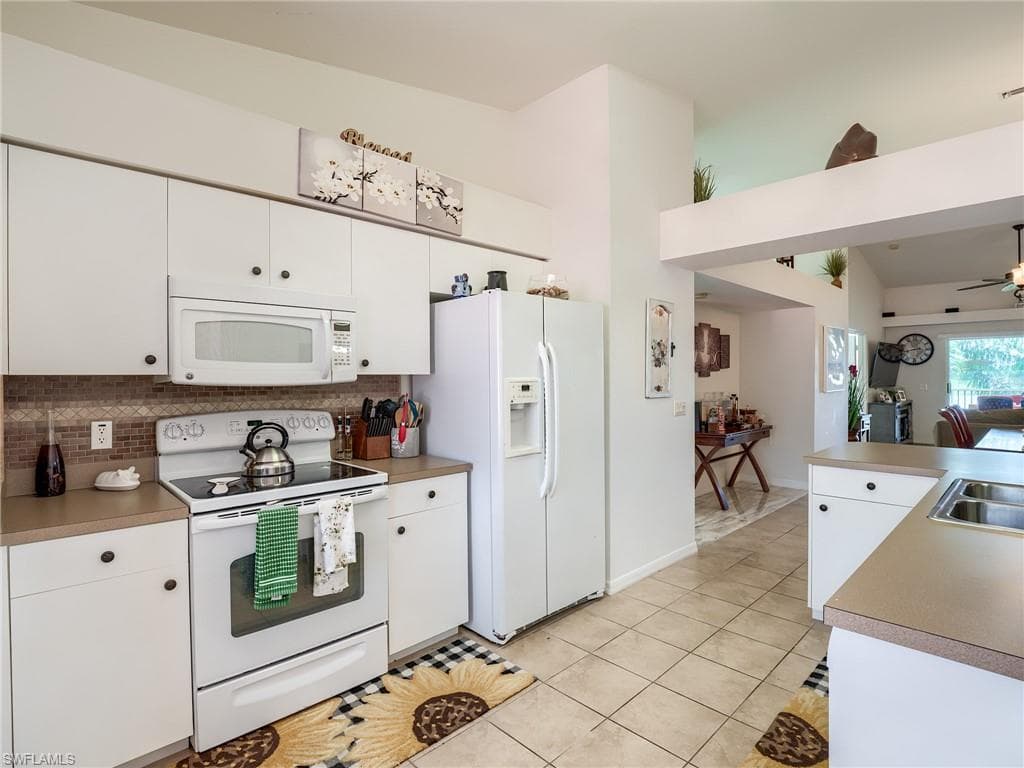 Kitchen with white appliances, white cabinets, decorative backsplash, light countertops, and light tile patterned floors