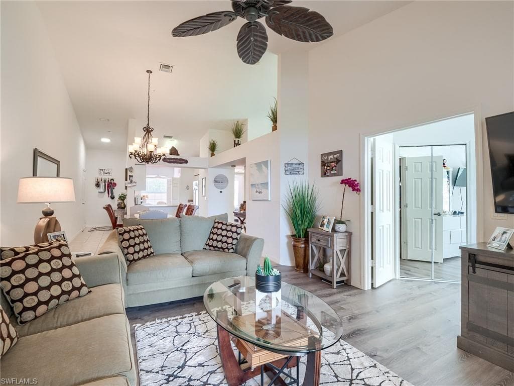 Living room with wood finished floors, ceiling fan, a high ceiling, and a chandelier