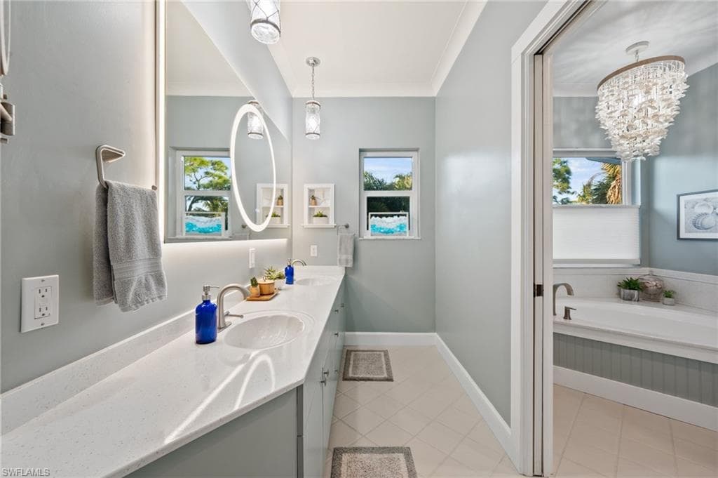 Bathroom with double vanity, a chandelier, crown molding, and a soaker tub with separate shower stall
