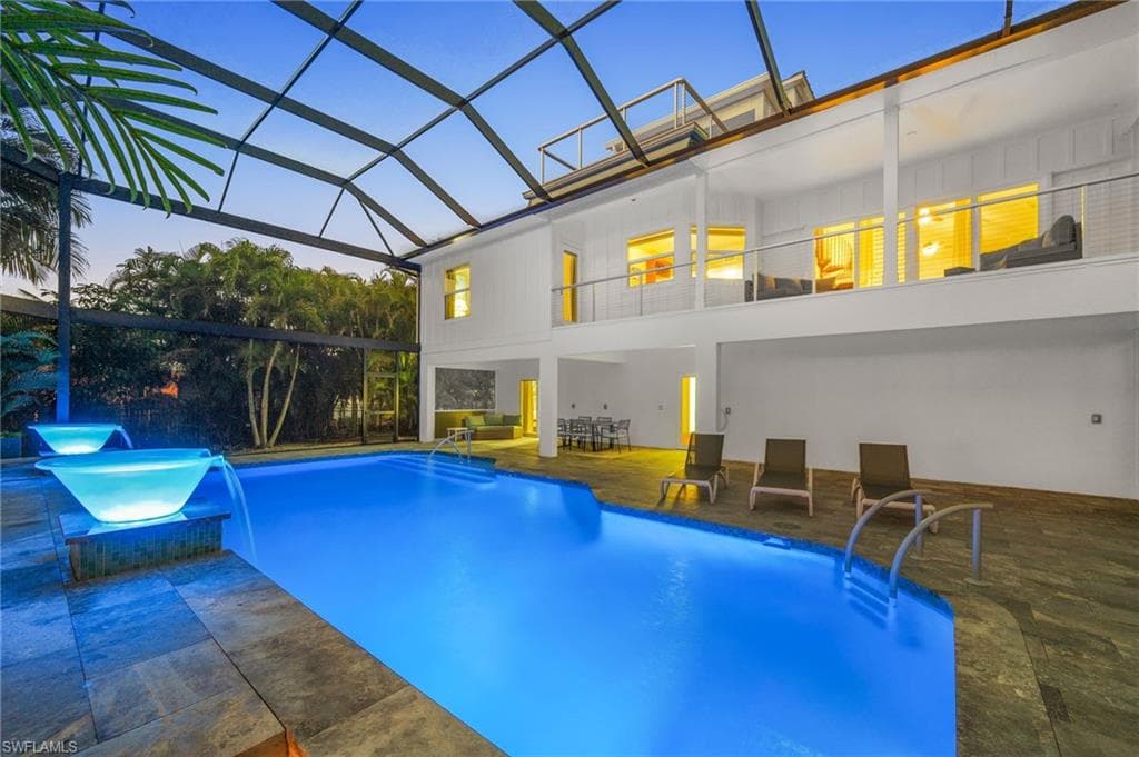Pool at dusk with an infinity fountains, a lanai, and a patio
