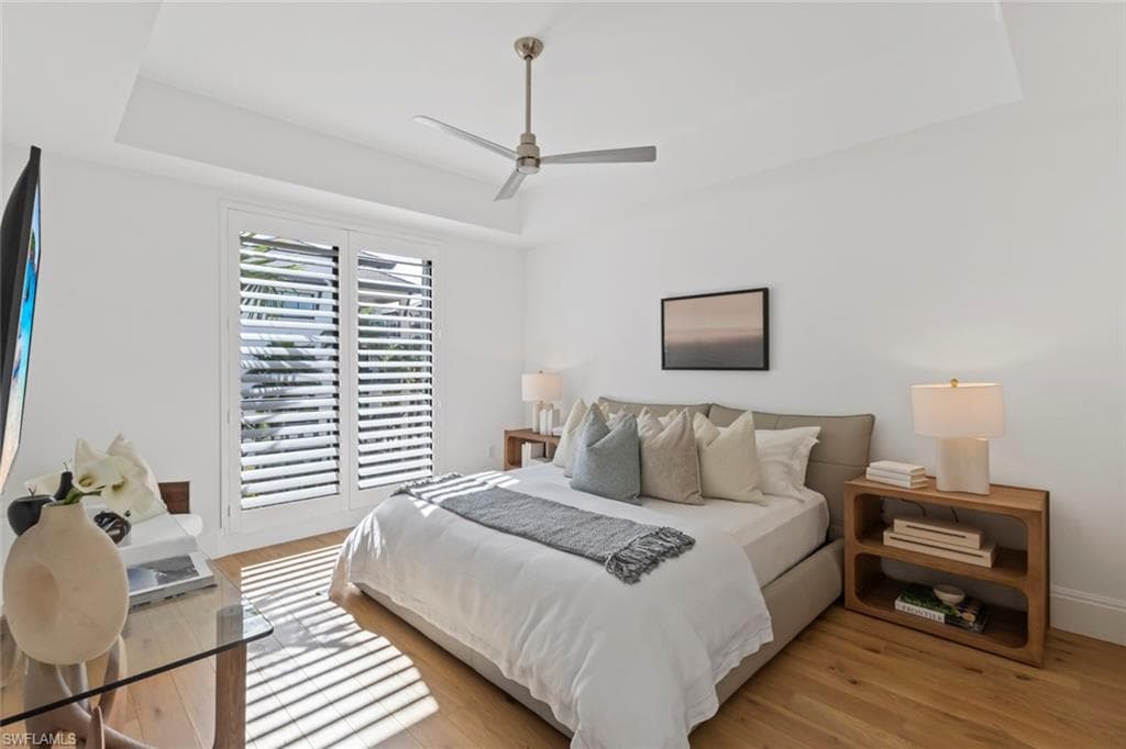 Bedroom featuring a tray ceiling, light wood-style flooring, and ceiling fan