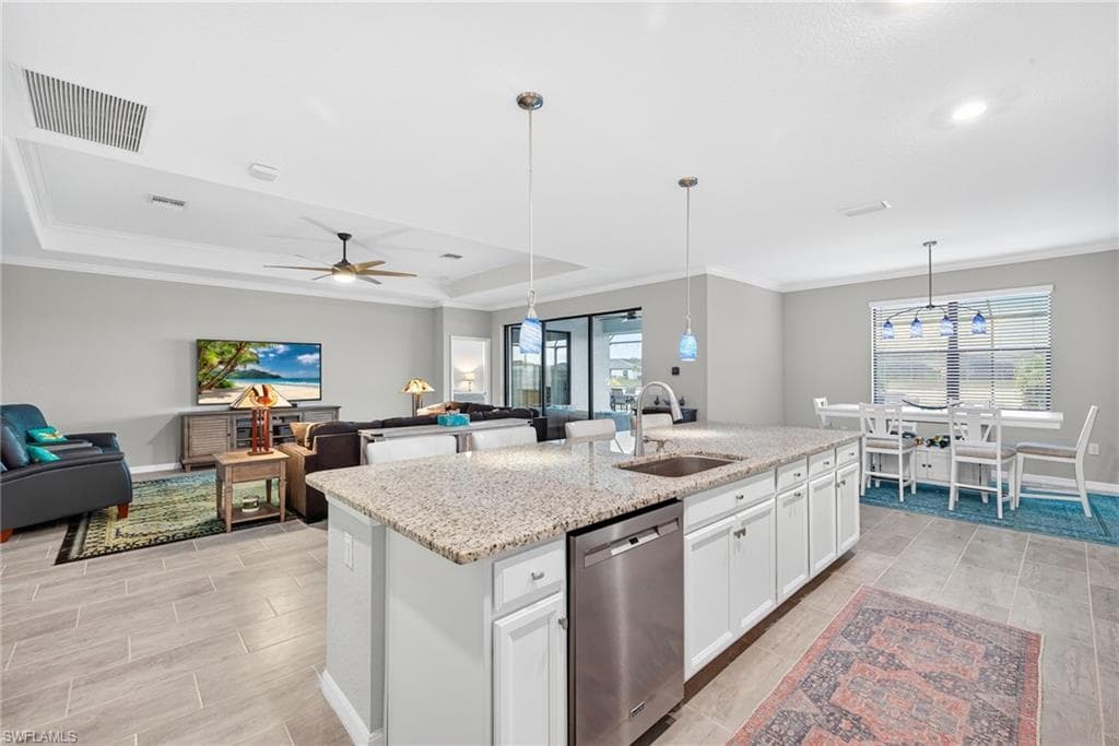 Kitchen featuring dishwasher, white cabinets, open floor plan, light stone counters, and crown molding