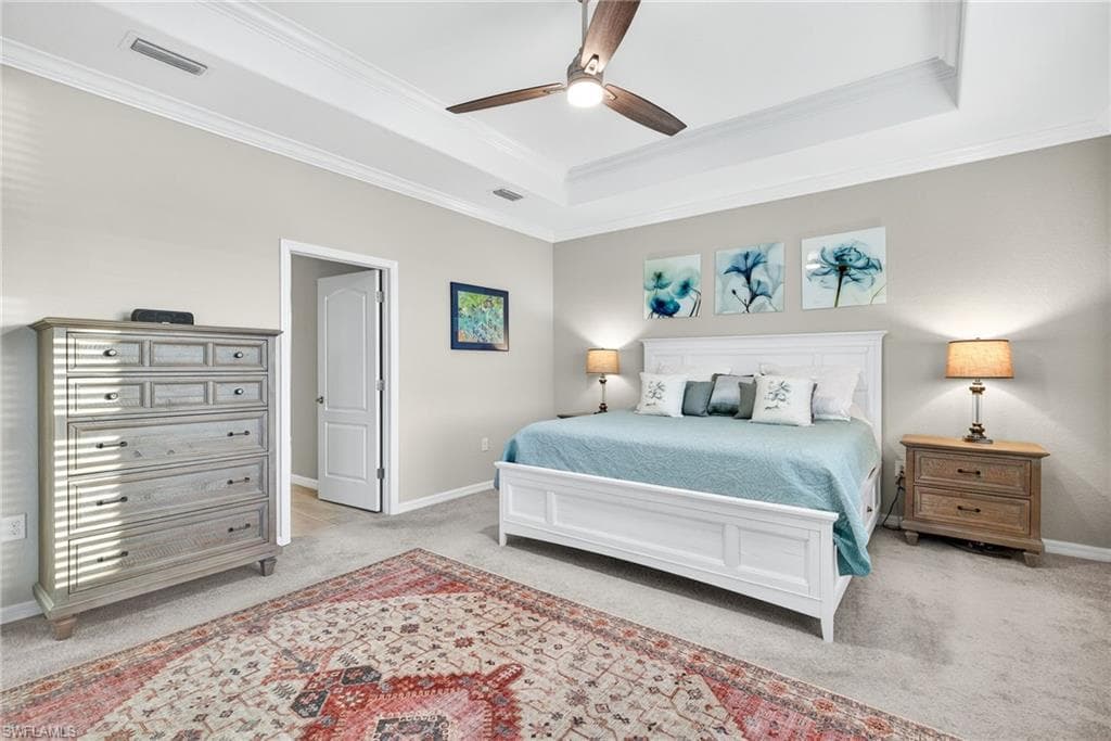 Bedroom featuring light carpet, ceiling fan, a tray ceiling, and crown molding