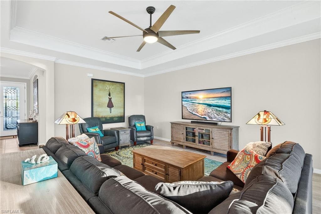 Living area featuring arched walkways, crown molding, a tray ceiling, and ceiling fan