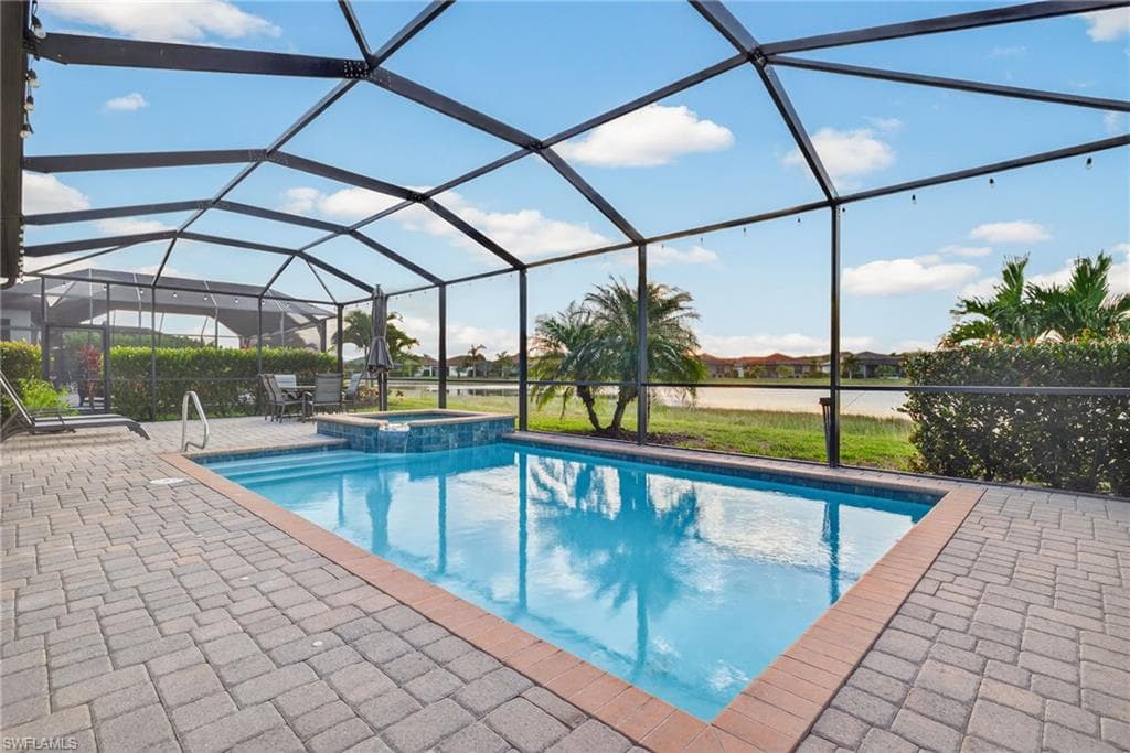 View of swimming pool featuring a sunroom, glass enclosure, a pool with connected hot tub, a water view, and a patio