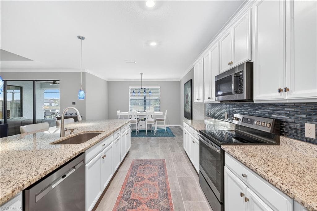 Kitchen featuring appliances with stainless steel finishes, white cabinetry, ornamental molding, pendant lighting, and light stone countertops