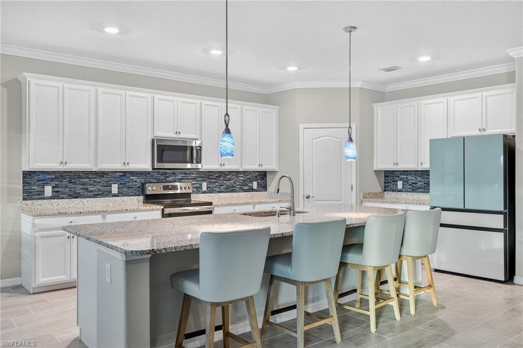 Kitchen featuring a breakfast bar area, tasteful backsplash, white cabinets, appliances with stainless steel finishes, and crown molding