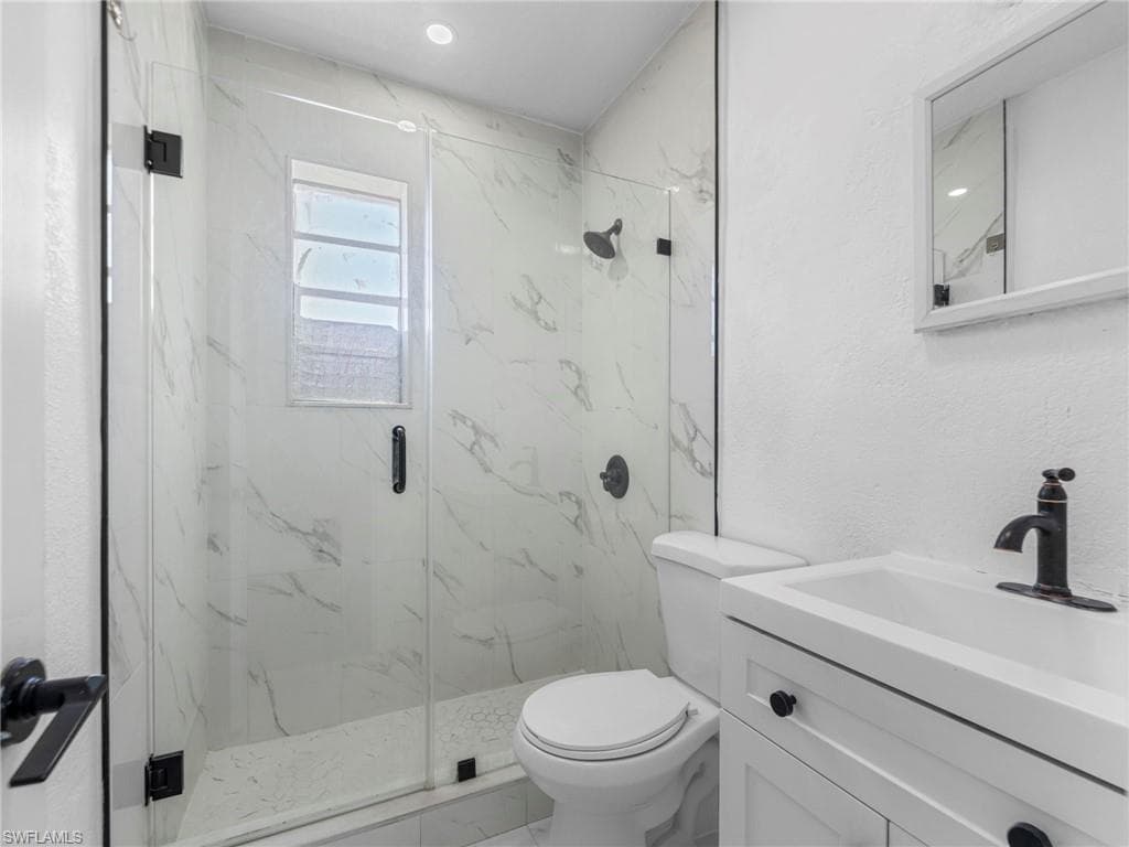 Full bath with vanity, a textured wall, a marble finish shower, and marble look tile flooring