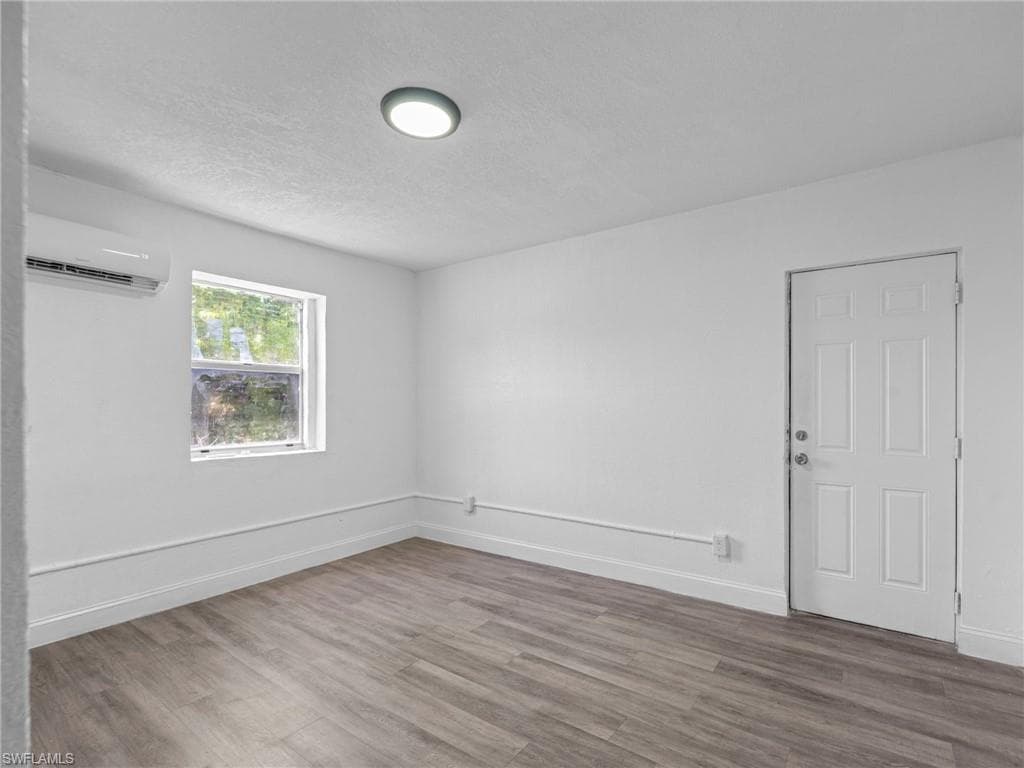 Spare room with a textured ceiling, wood finished floors, and a wall mounted air conditioner