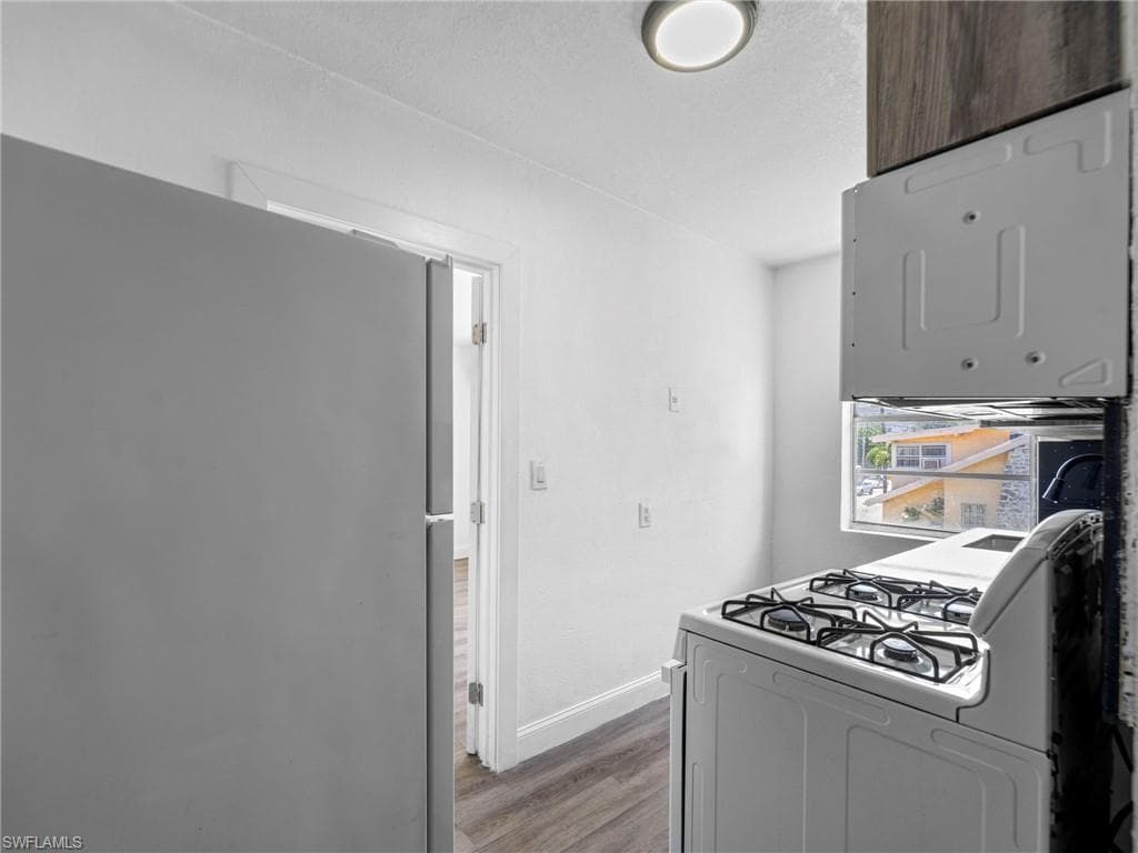 Kitchen featuring freestanding refrigerator, white gas range oven, wood finished floors, and a textured ceiling