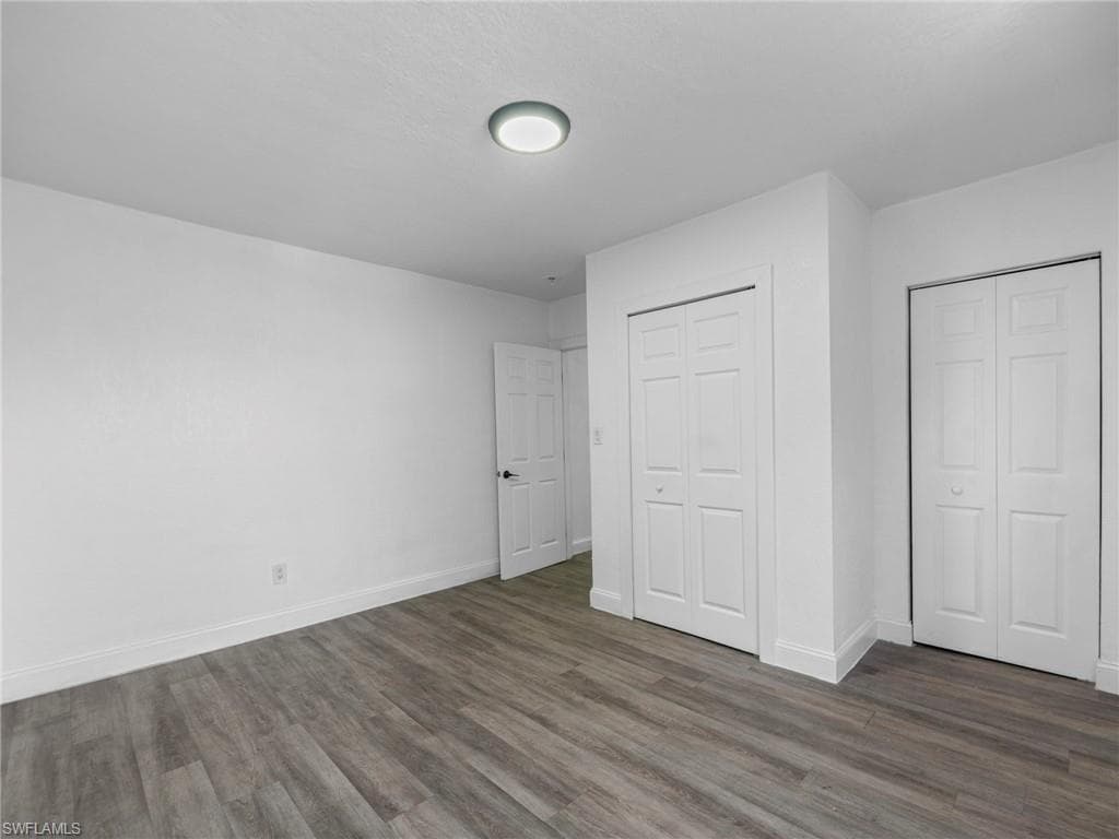 Unfurnished bedroom featuring dark wood-style flooring and two closets