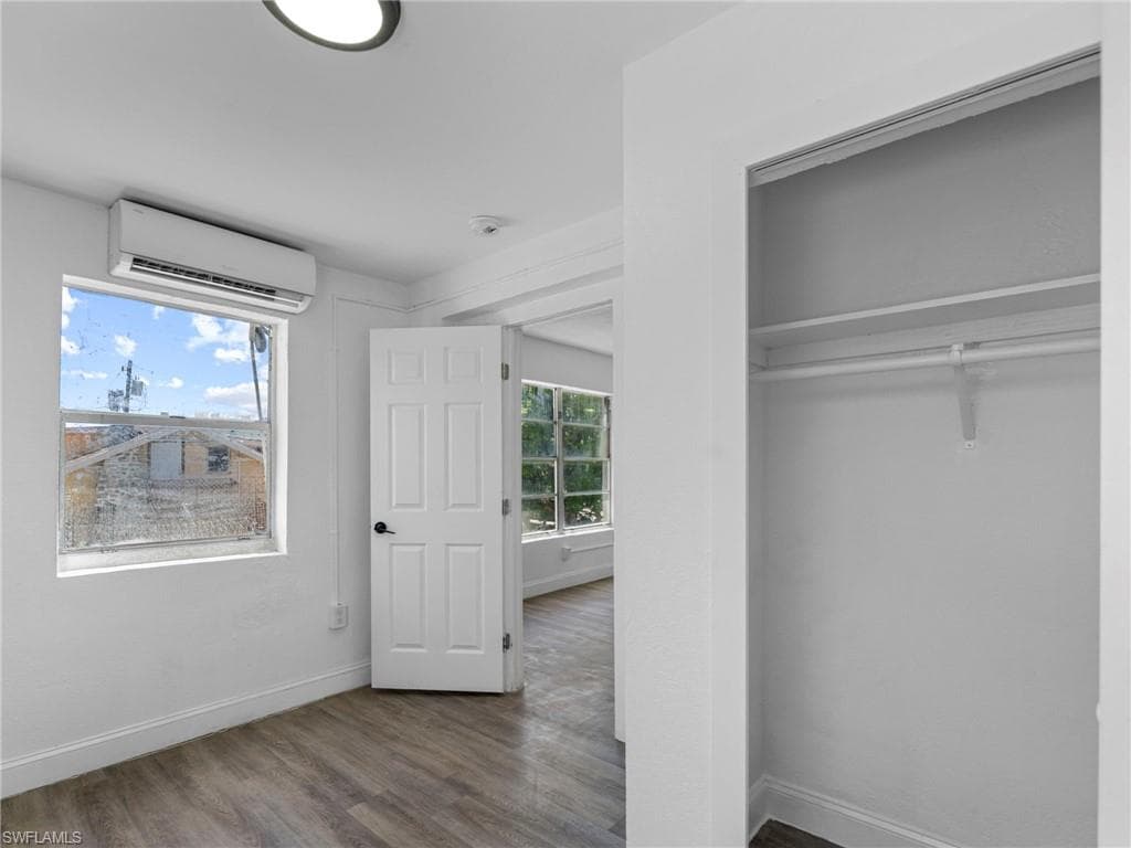 Unfurnished bedroom featuring a wall mounted AC, dark wood-style flooring, and a closet