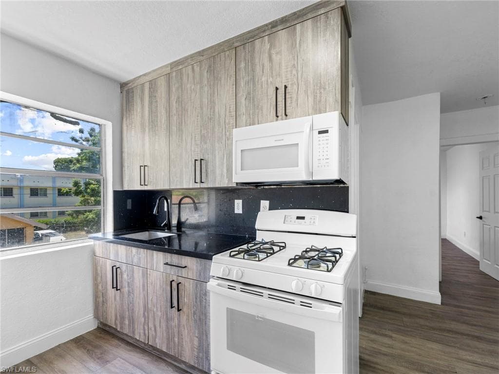 Kitchen with white appliances, dark wood-type flooring, tasteful backsplash, and dark stone countertops