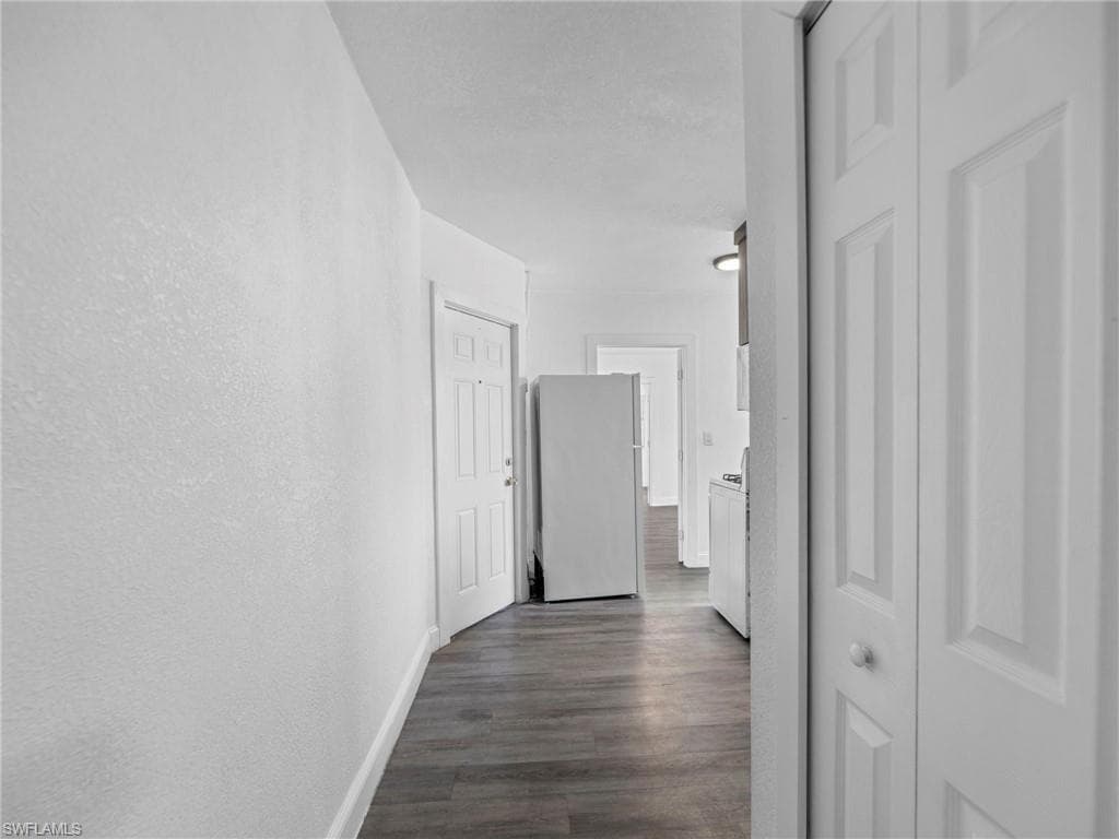 Hallway featuring dark wood-type flooring, a textured wall, and a textured ceiling
