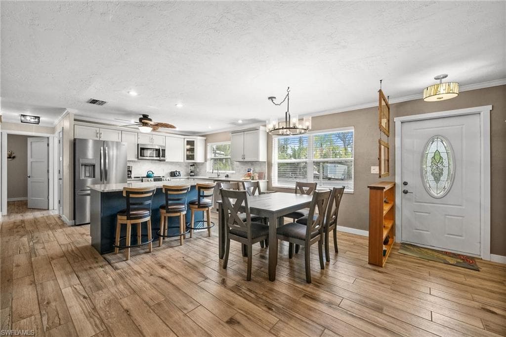 Dining area featuring ceiling fan, crown molding, a chandelier, a textured ceiling, and light wood-style floors