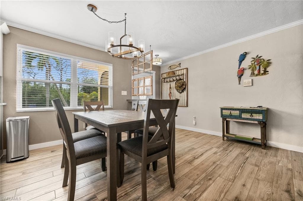 Dining space with ornamental molding, light wood finished floors, and a chandelier