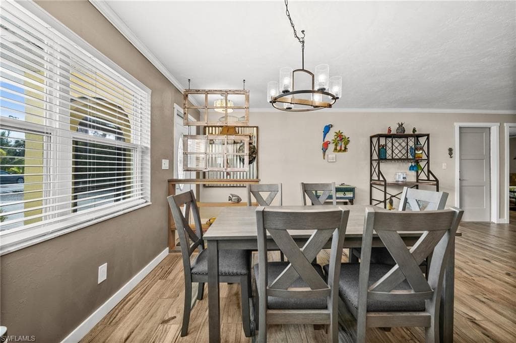 Dining area with light wood-type flooring, ornamental molding, and a chandelier