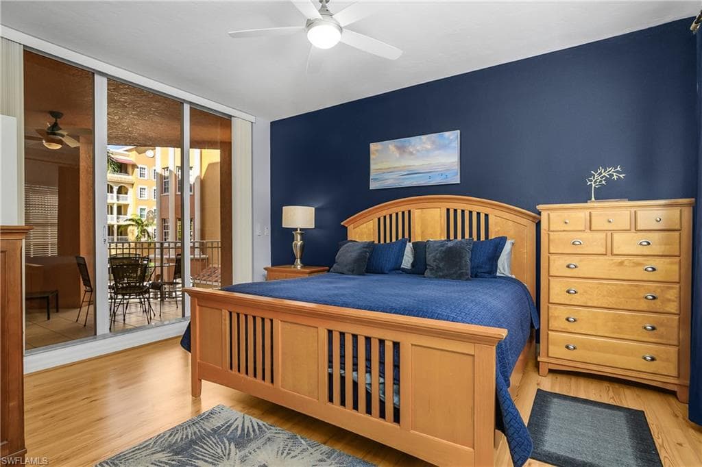 Bedroom featuring wood finished floors, a wall of windows, access to outside, ceiling fan, and an accent wall