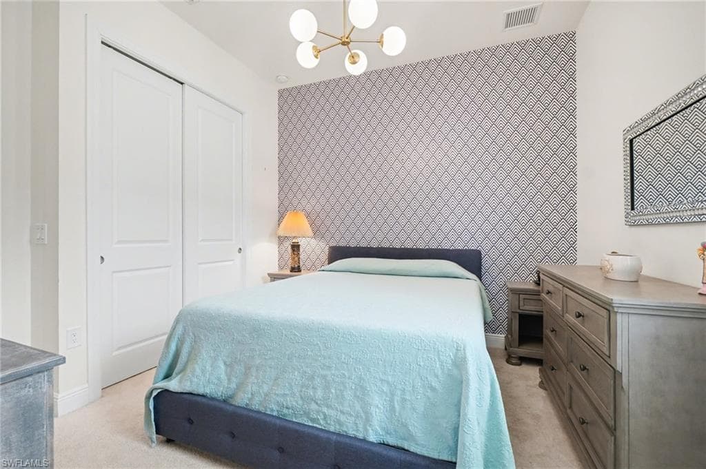 Bedroom with an accent wall, a chandelier, a closet, wallpapered walls, and light colored carpet