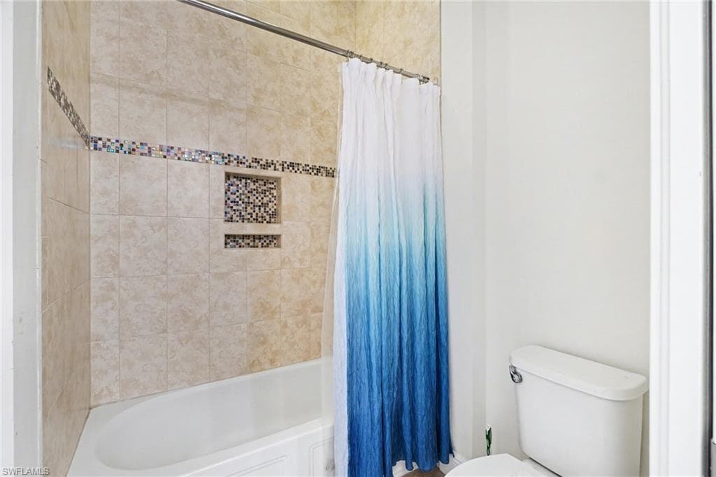Full bathroom featuring shower / bath combination with curtain and toilet