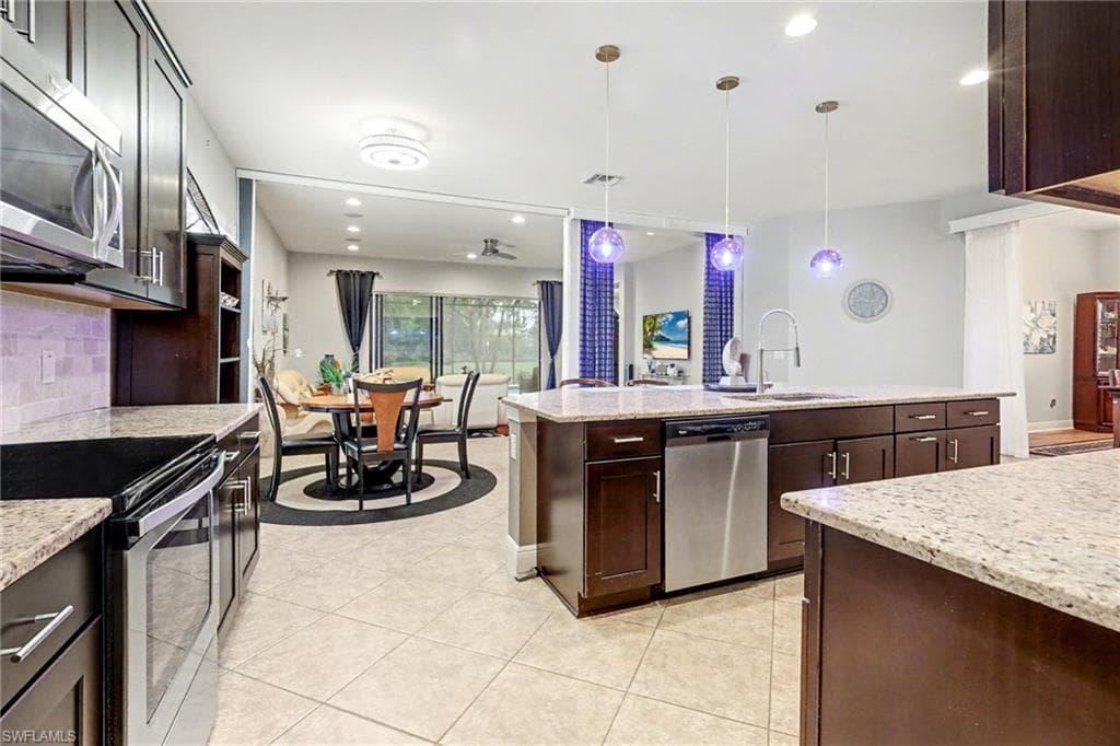 Kitchen with dark brown cabinets, appliances with stainless steel finishes, light stone countertops, pendant lighting, and recessed lighting