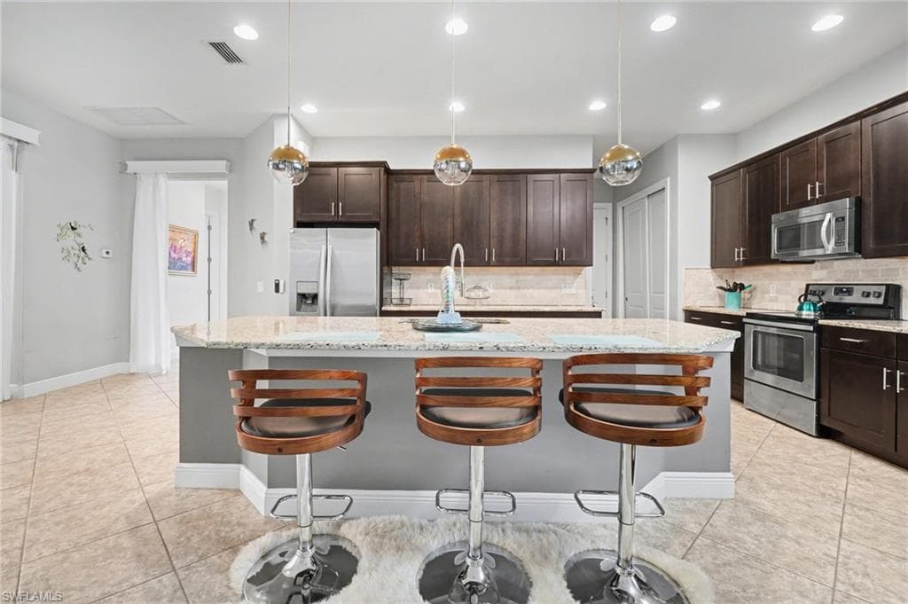 Kitchen with hanging light fixtures, stainless steel appliances, dark brown cabinets, a kitchen bar, and recessed lighting