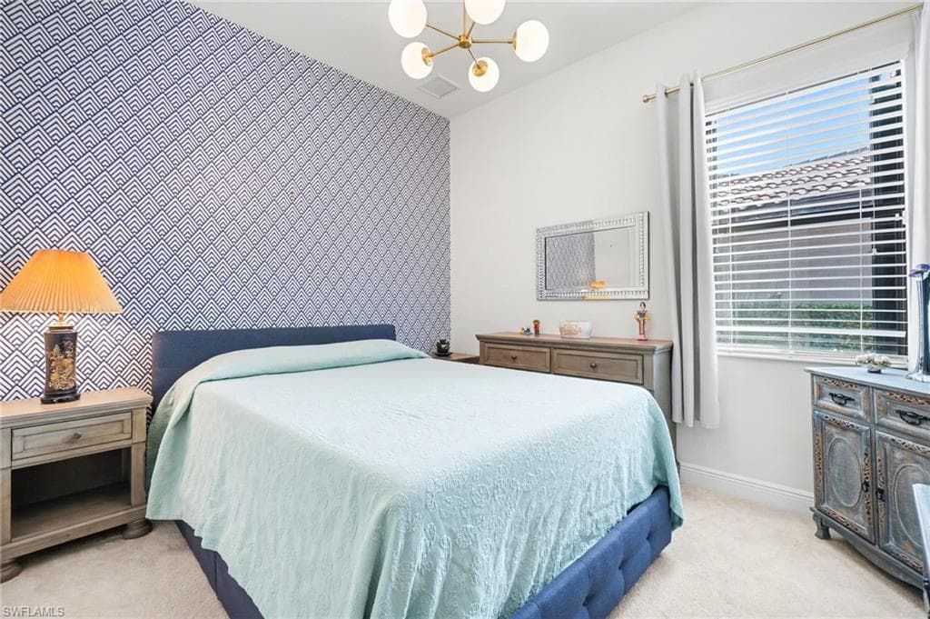 Bedroom featuring an accent wall, light carpet, a chandelier, and wallpapered walls