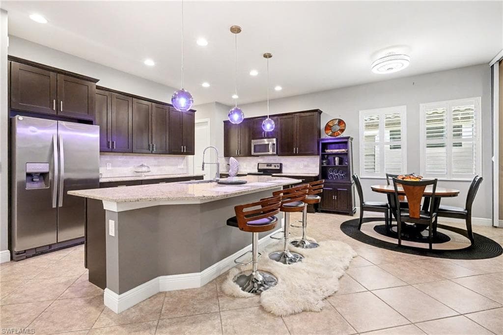 Kitchen with a kitchen breakfast bar, stainless steel appliances, dark brown cabinets, pendant lighting, and an island with sink