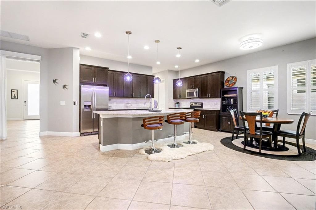 Kitchen featuring dark brown cabinetry, a breakfast bar, appliances with stainless steel finishes, pendant lighting, and a kitchen island with sink