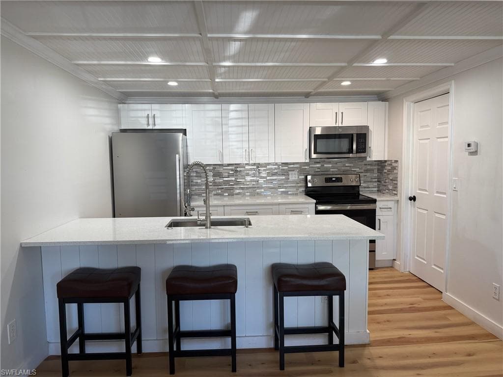 Kitchen with breakfast bar, stainless steel appliances, white cabinets, and light stone countertops