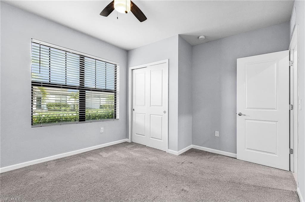 Guest bedroom with large window featuring light colored carpet, a ceiling fan, and a closet