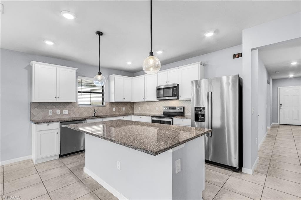 Kitchen featuring stainless steel appliances, granite counters, pendant lighting, white cabinetry, and a center island