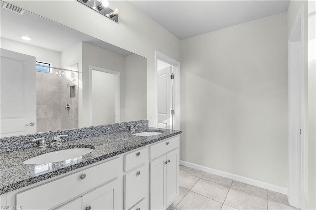 Bathroom with double vanity, light tile patterned flooring, and tiled shower