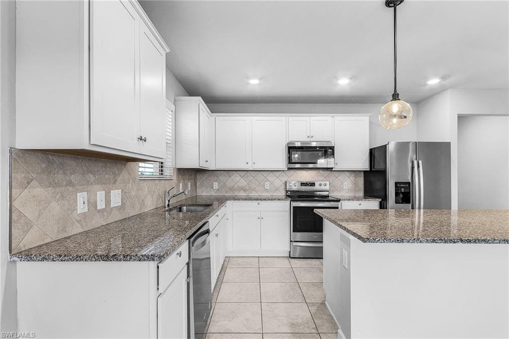 Kitchen with appliances with stainless steel finishes, white cabinets, granite counters, pendants, and recessed lighting