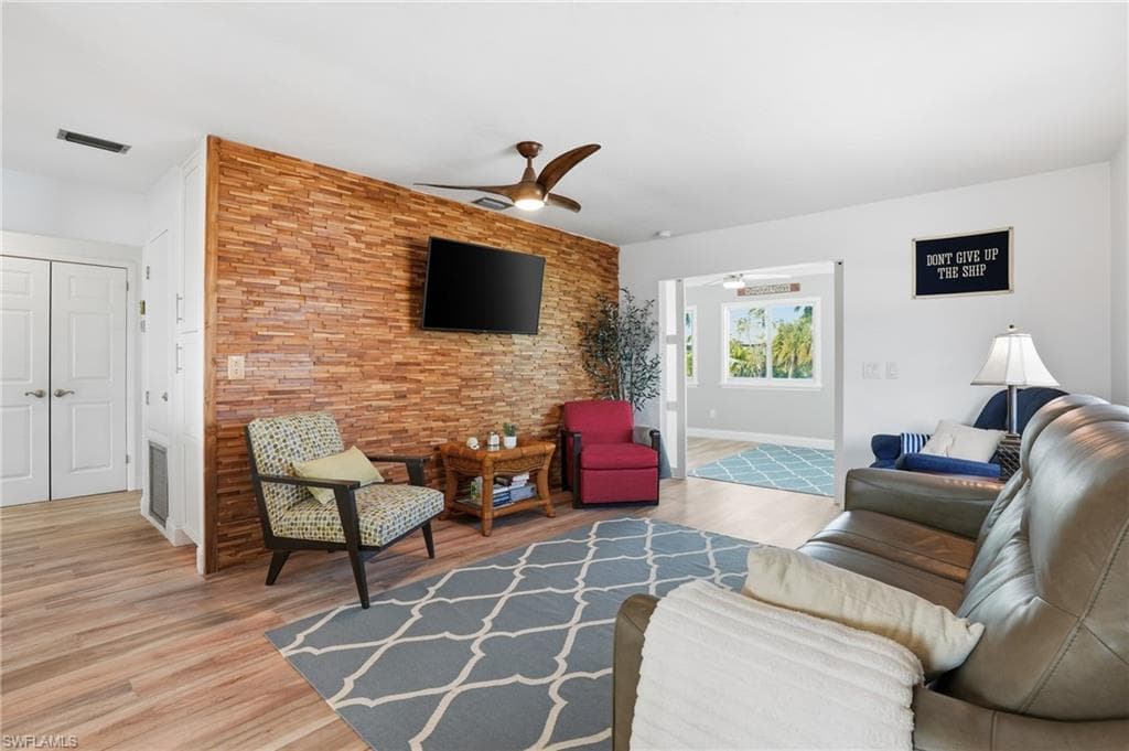 Living area with ceiling fan, an accent wall, and light wood-style flooring - Virtually Edited Image