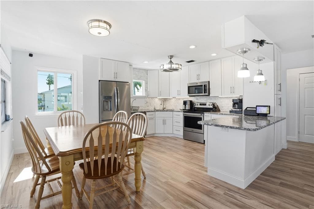 Kitchen with dark stone counters, appliances with stainless steel finishes, and white cabinetry - Virtually Edited Image