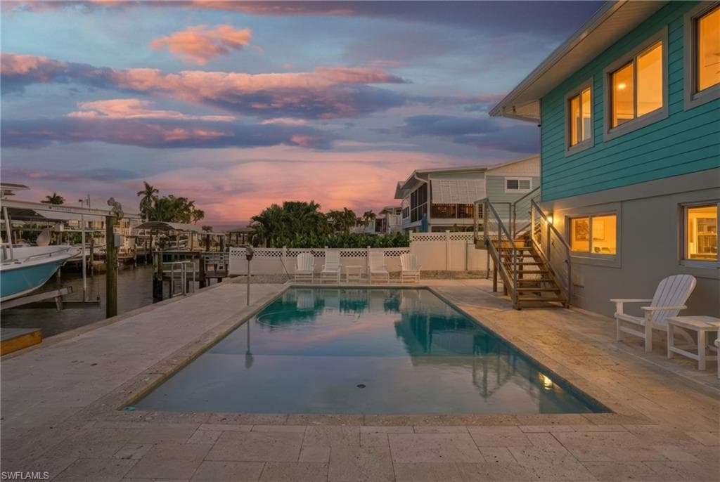 Pool at dusk with a patio, stairway, boat lift, a boat dock, and a water view - Virtually Edited Image