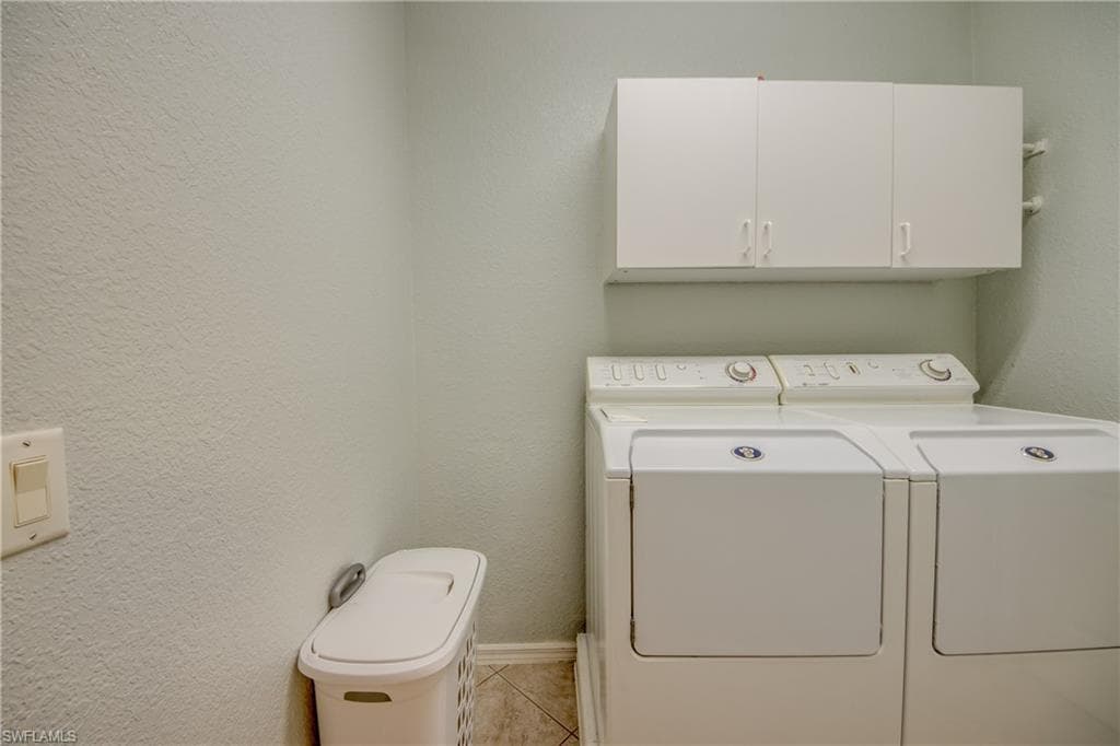 Laundry area with a textured wall, independent washer and dryer, light tile patterned floors, and cabinet space