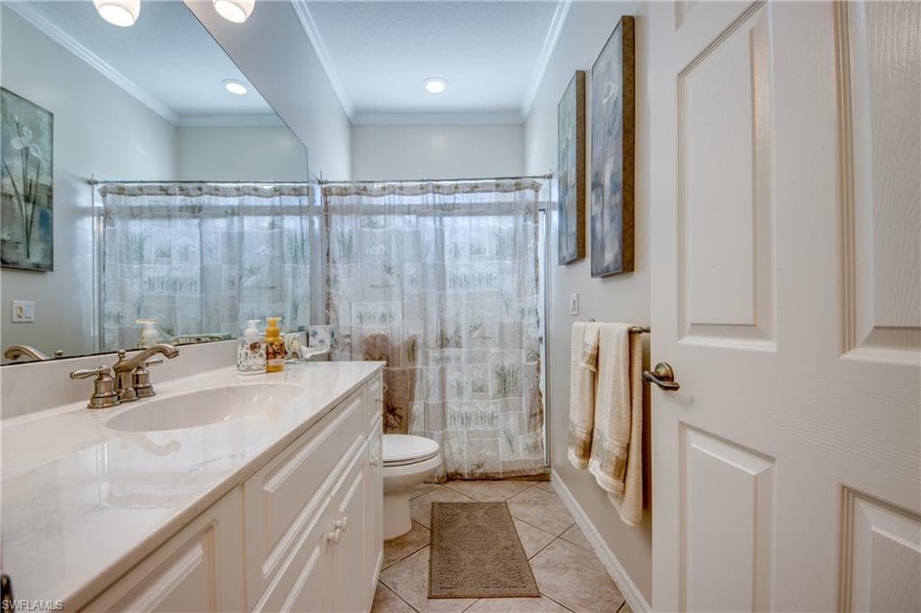 Full bathroom featuring a shower with shower curtain, crown molding, light tile patterned floors, and vanity
