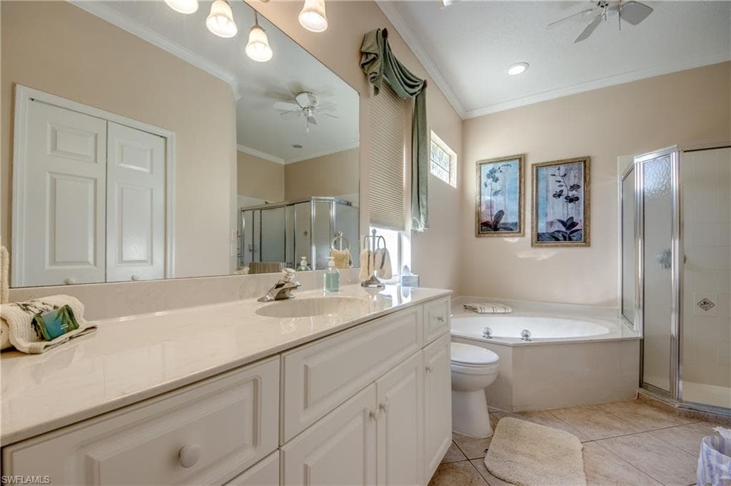 Bathroom with a ceiling fan, vanity, ornamental molding, a stall shower, and a garden tub