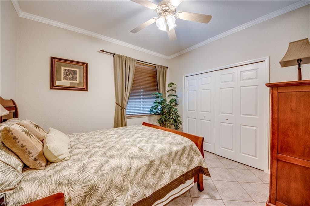 Bedroom with crown molding, ceiling fan, light tile patterned floors, and a closet