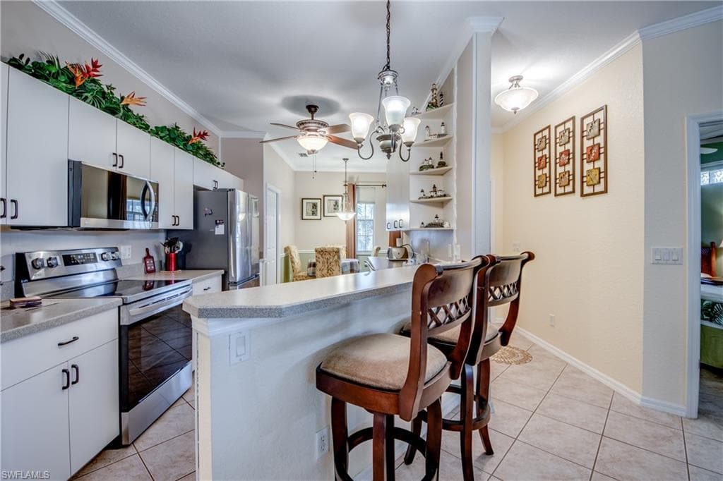 Kitchen featuring a kitchen breakfast bar, appliances with stainless steel finishes, decorative light fixtures, white cabinetry, and ornamental molding