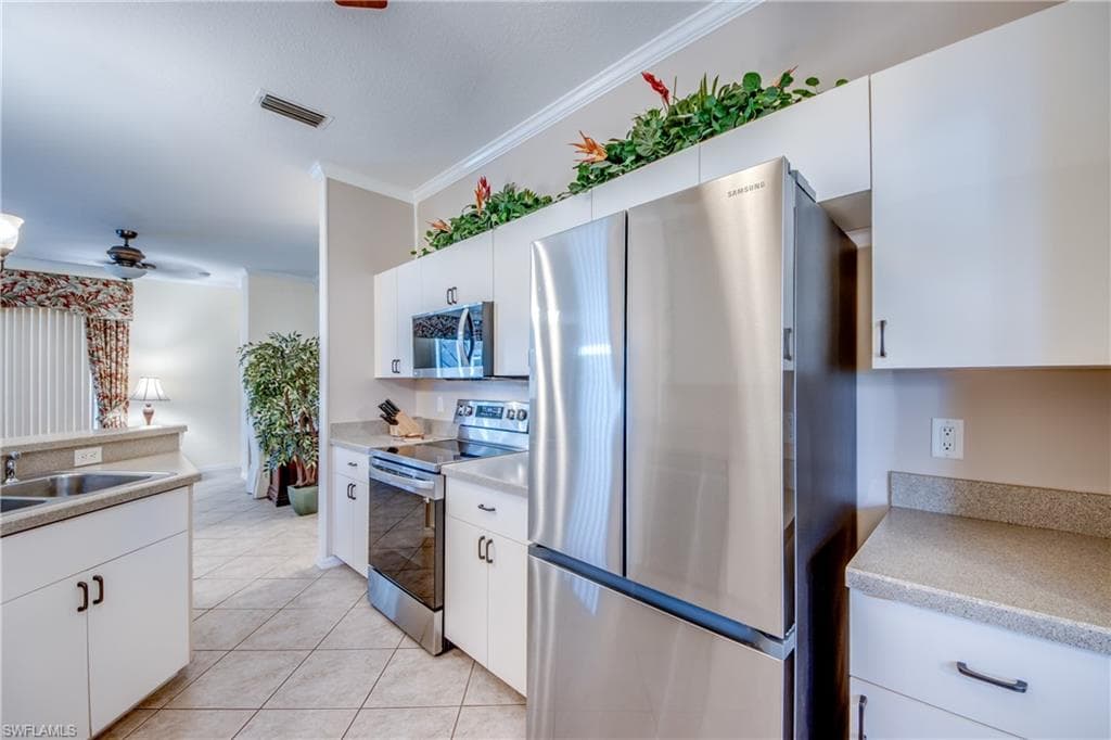 Kitchen featuring stainless steel appliances, ornamental molding, ceiling fan, white cabinets, and light tile patterned floors