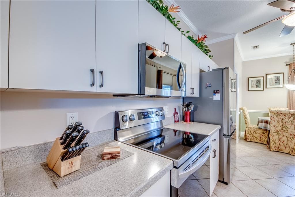 Kitchen featuring appliances with stainless steel finishes, crown molding, light tile patterned flooring, white cabinets, and ceiling fan